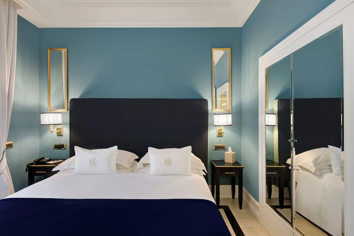 Une chambre d’hôtel avec un grand lit, des tables de chevet, une commode, un miroir et une armoire.