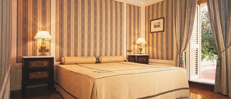 A hotel room with a large bed, two bedside tables with lamps, a patterned rug, and a view of greenery outside.