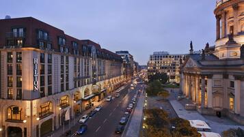 A hotel with a prominent 'Hilton' sign, a wide street with parked cars, and a classical building with columns in the background.