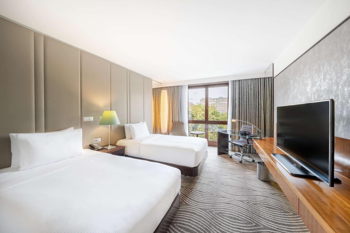 A hotel room with two beds, a desk with a chair, a television, and a window with curtains.