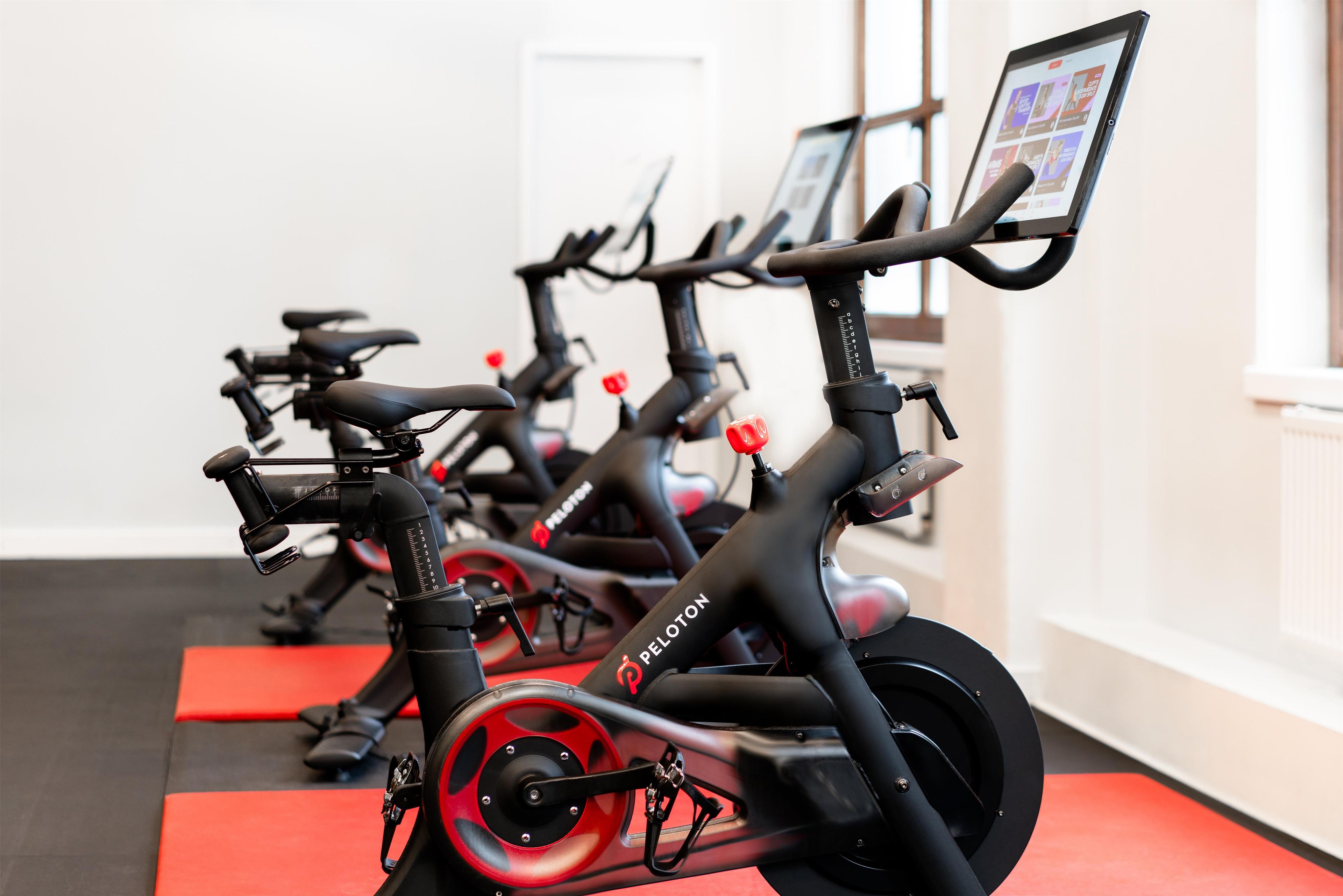 Une rangée de vélos d’appartement dans une pièce dont le sol est recouvert d’un tapis rouge.