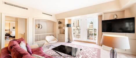 Una sala de estar moderna con un televisor de pantalla plana grande, un sofá de terciopelo rojo, una mesa de centro de vidrio y vistas de un paisaje urbano a través de ventanas amplias.