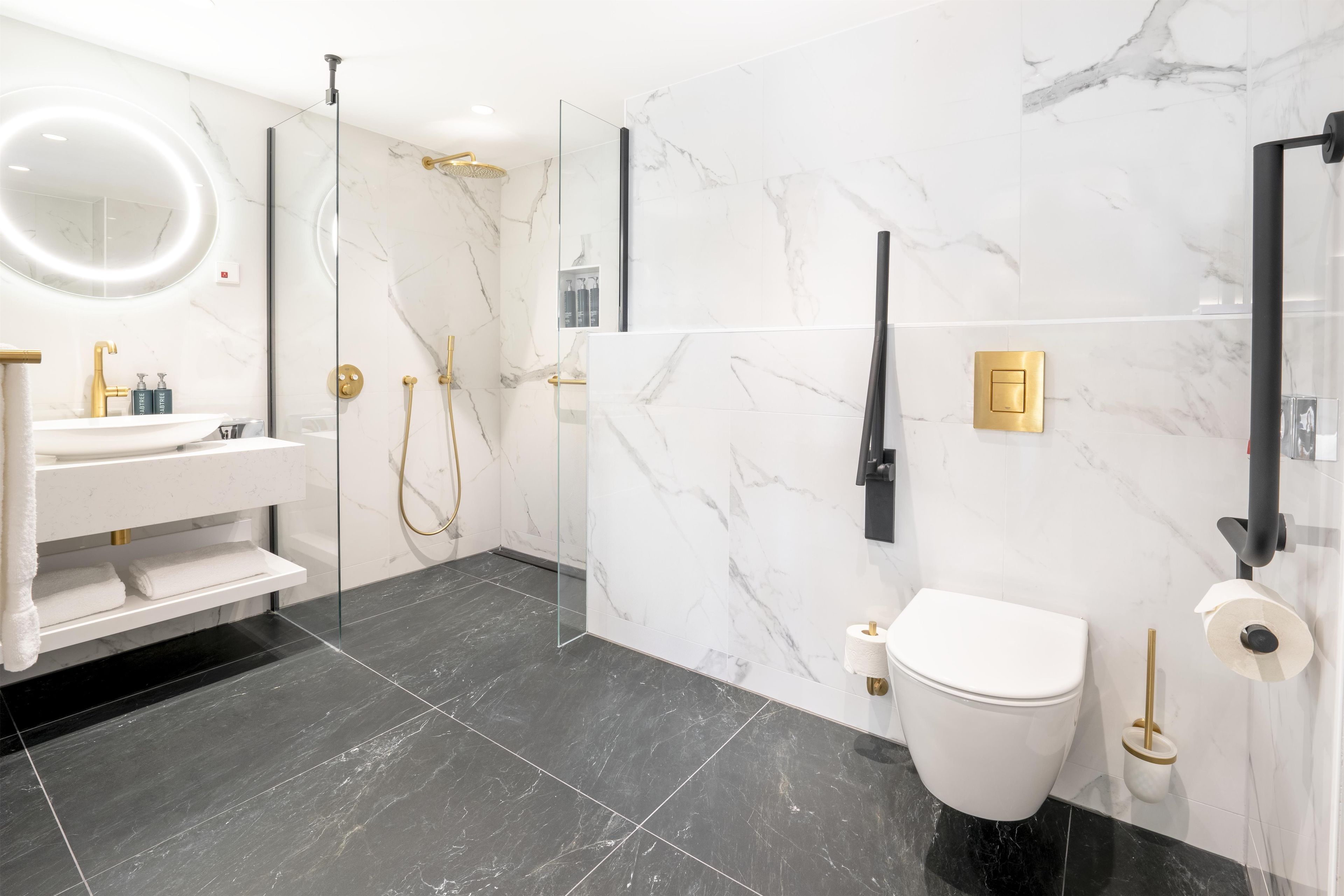 Un bagno moderno con doccia vetrata, lavandino bianco con dettagli dorati, un water e pareti in marmo.