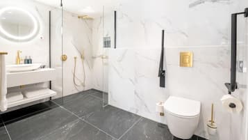 Un bagno moderno con doccia vetrata, lavandino bianco con dettagli dorati, un water e pareti in marmo.