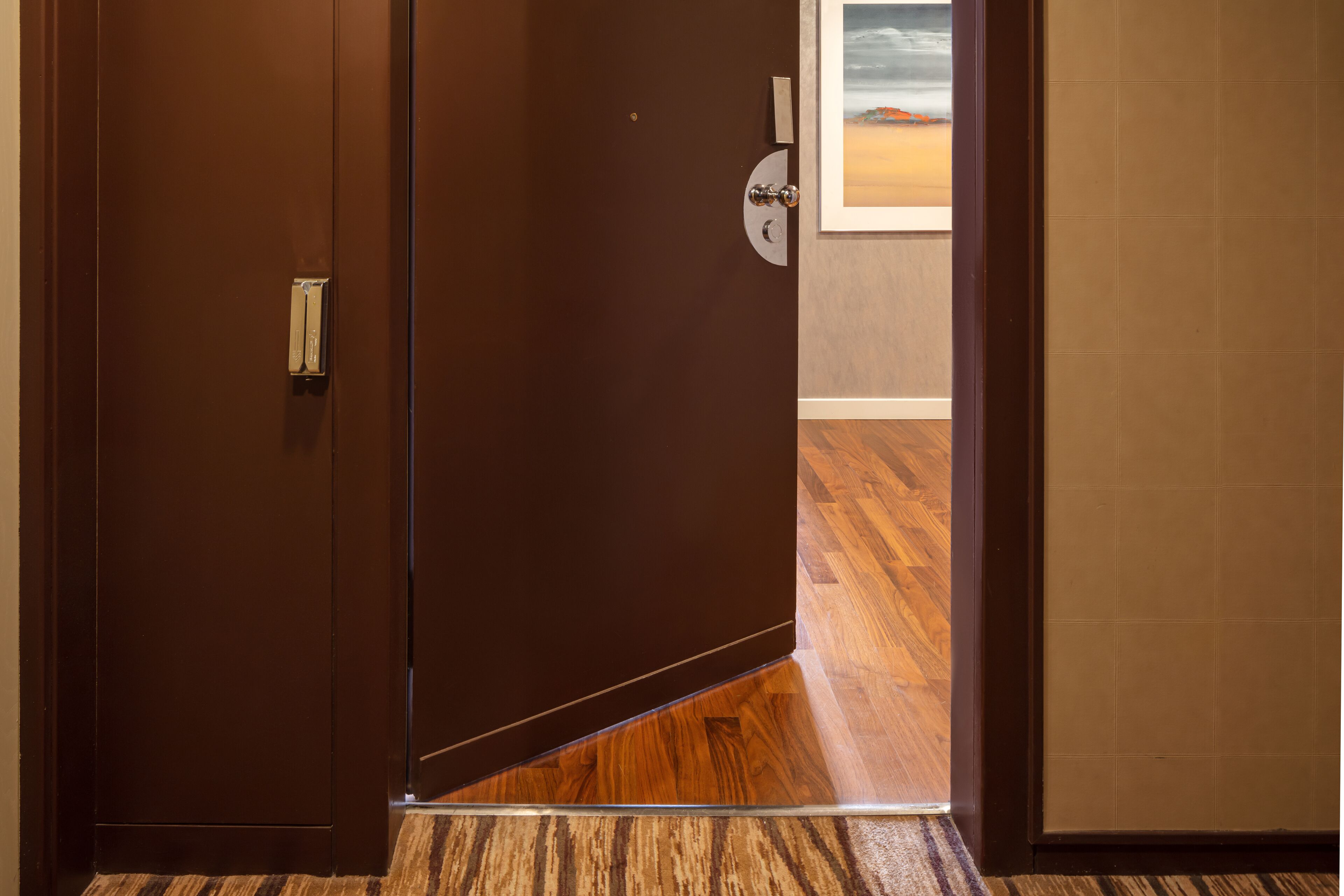 L’entrée d’une chambre d’hôtel avec un plancher en bois, une porte marron et une vue sur la plage par la fenêtre.