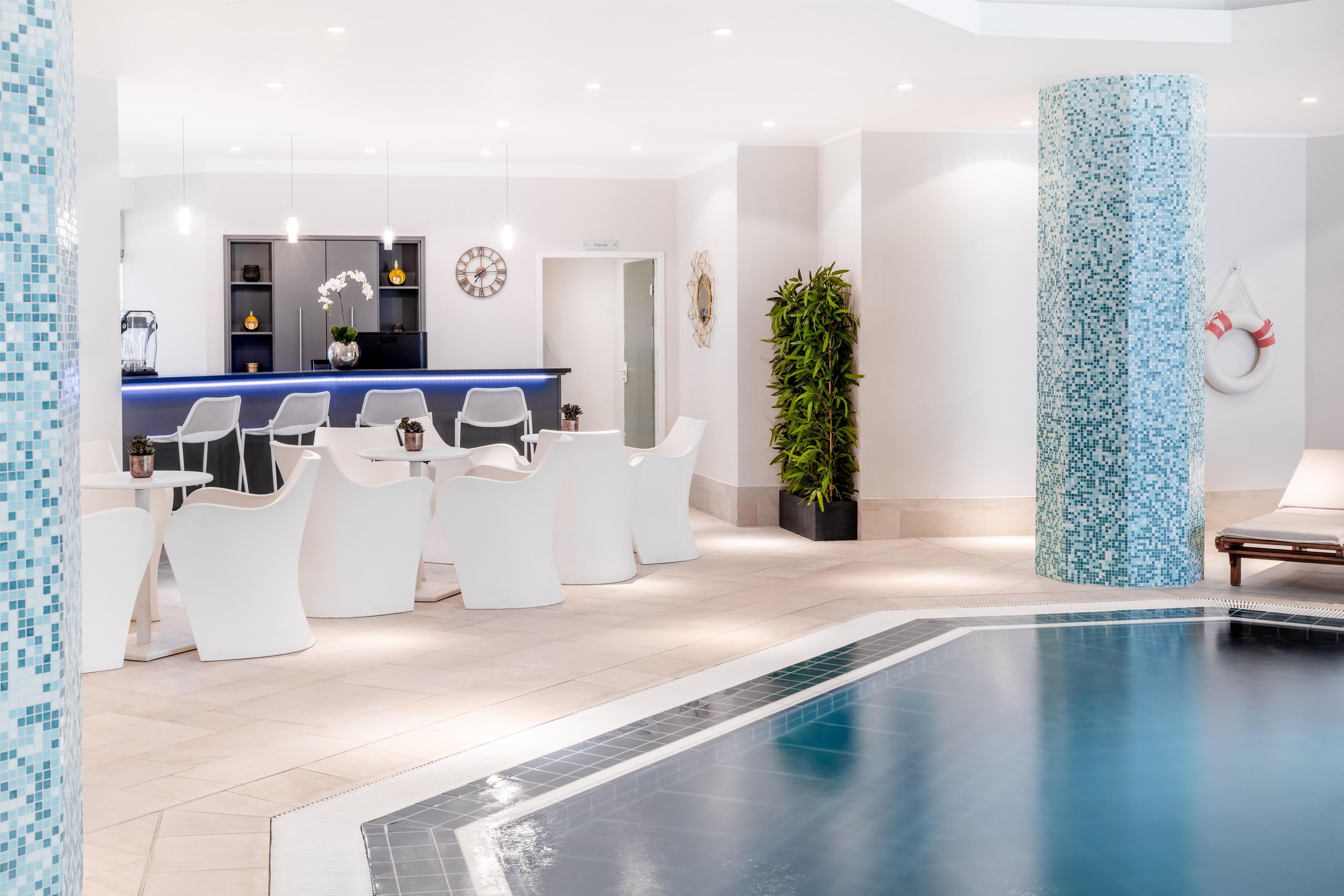 Un área interior de piscina moderna con una recepción, un espacio de descanso y una columna grande con mosaicos.
