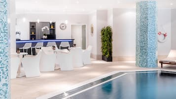 Un área interior de piscina moderna con una recepción, un espacio de descanso y una columna grande con mosaicos.