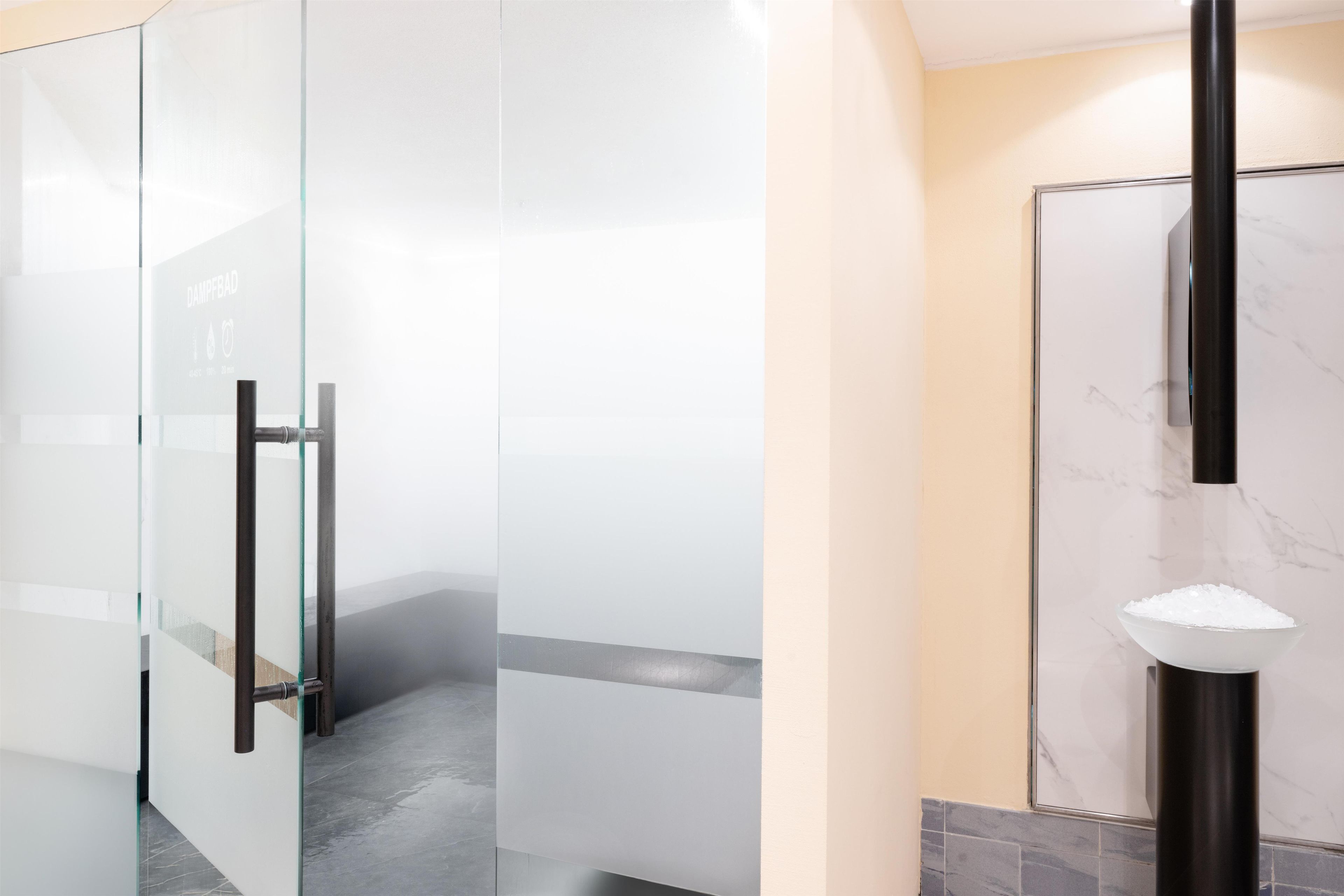 Un baño moderno con cabina de ducha de vidrio, lavamanos de mármol y puerta de vidrio con manija.