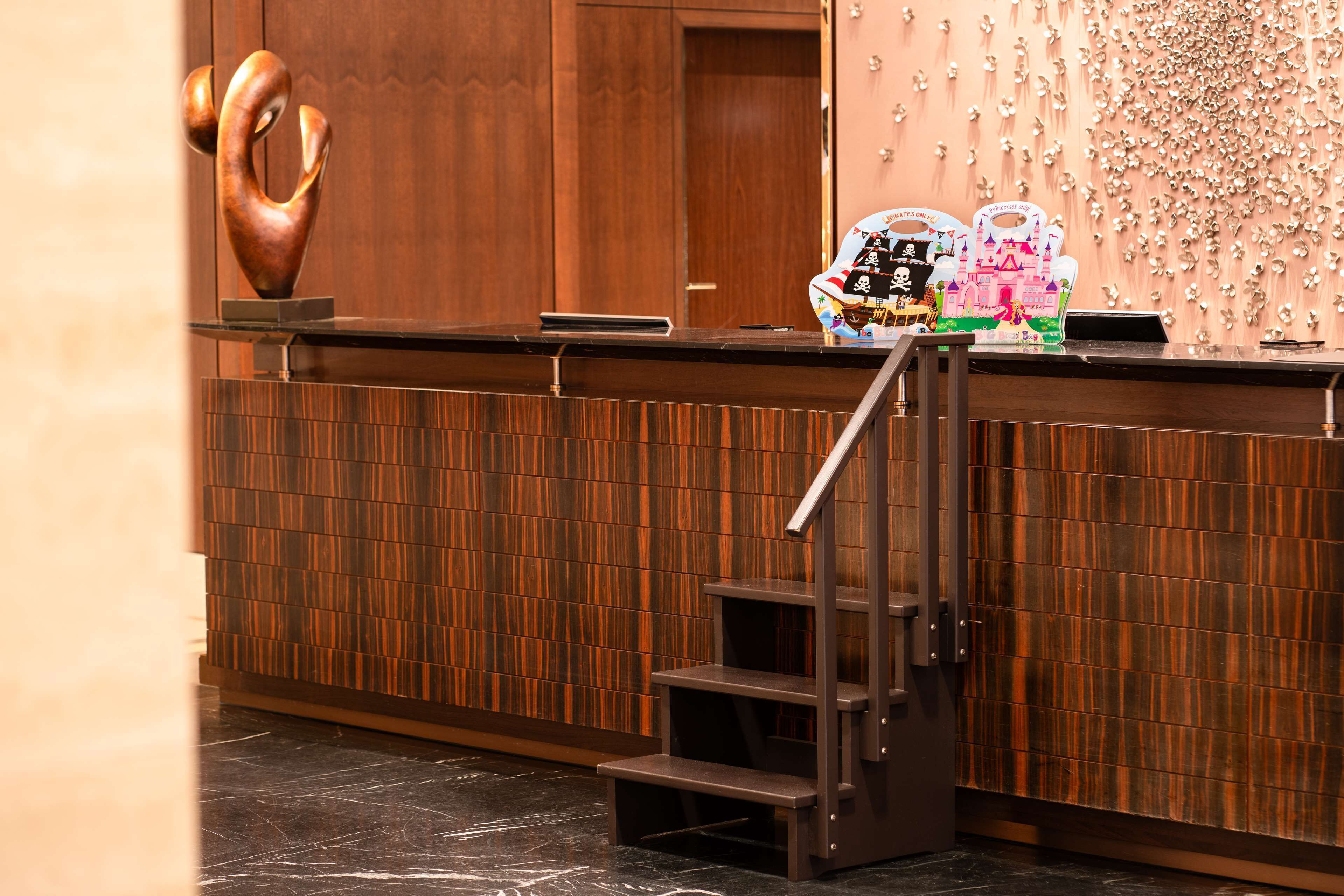 Un área de recepción con un mostrador de madera, una escalera de metal y una pared con un diseño decorativo.