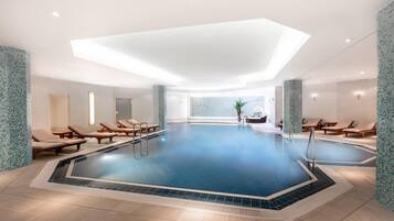 A large indoor swimming pool with lounge chairs and a high ceiling.