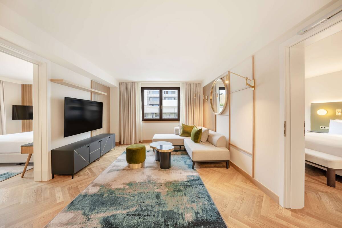 A modern hotel room with a flat-screen TV, a sofa, a coffee table, and a large window.