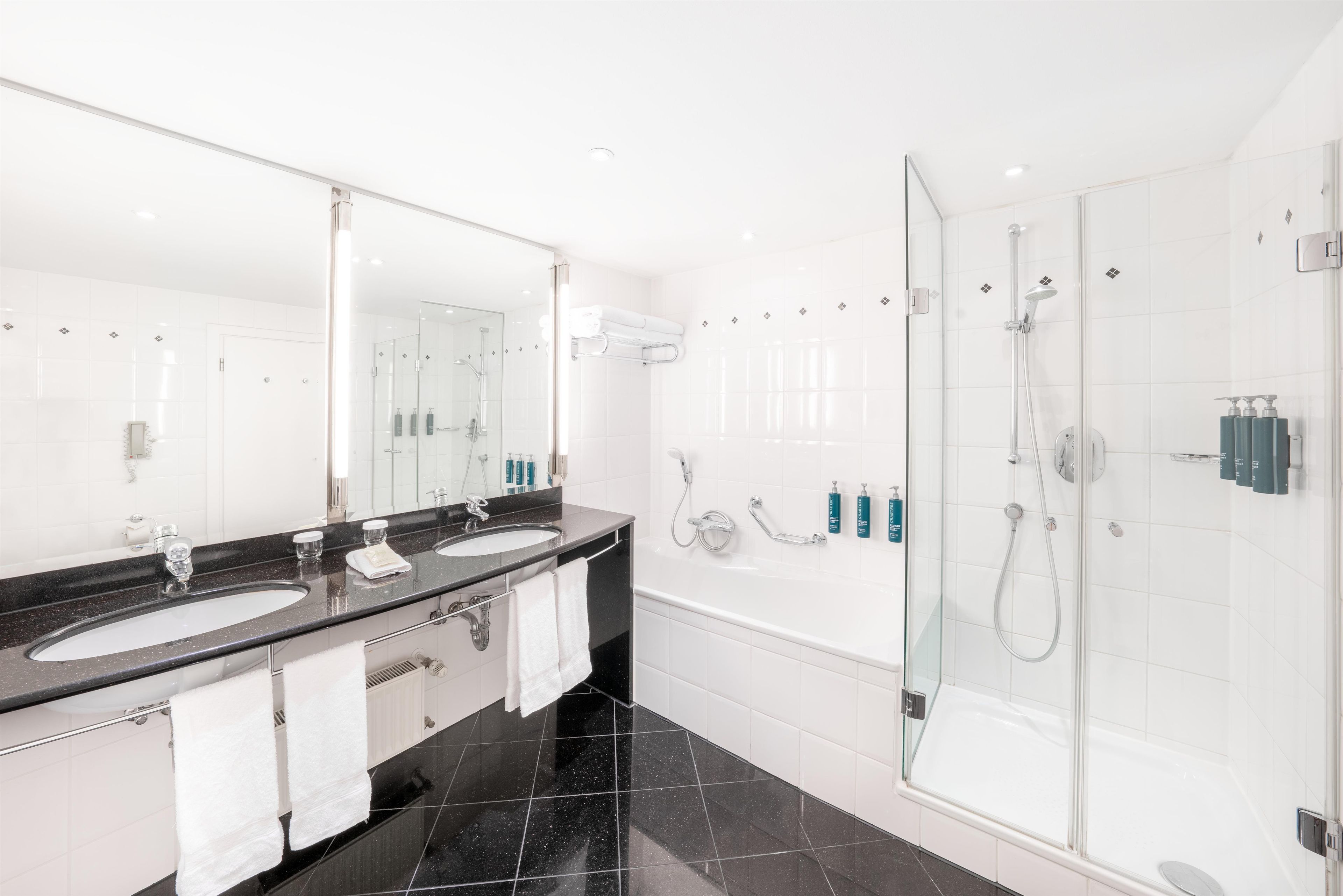 A modern bathroom with two sinks, a large mirror, and a glass-enclosed shower.