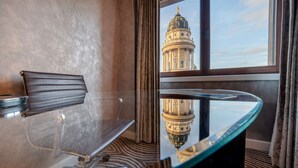 A hotel room with a modern chair, a glass table, and a view of a historic building through a window.