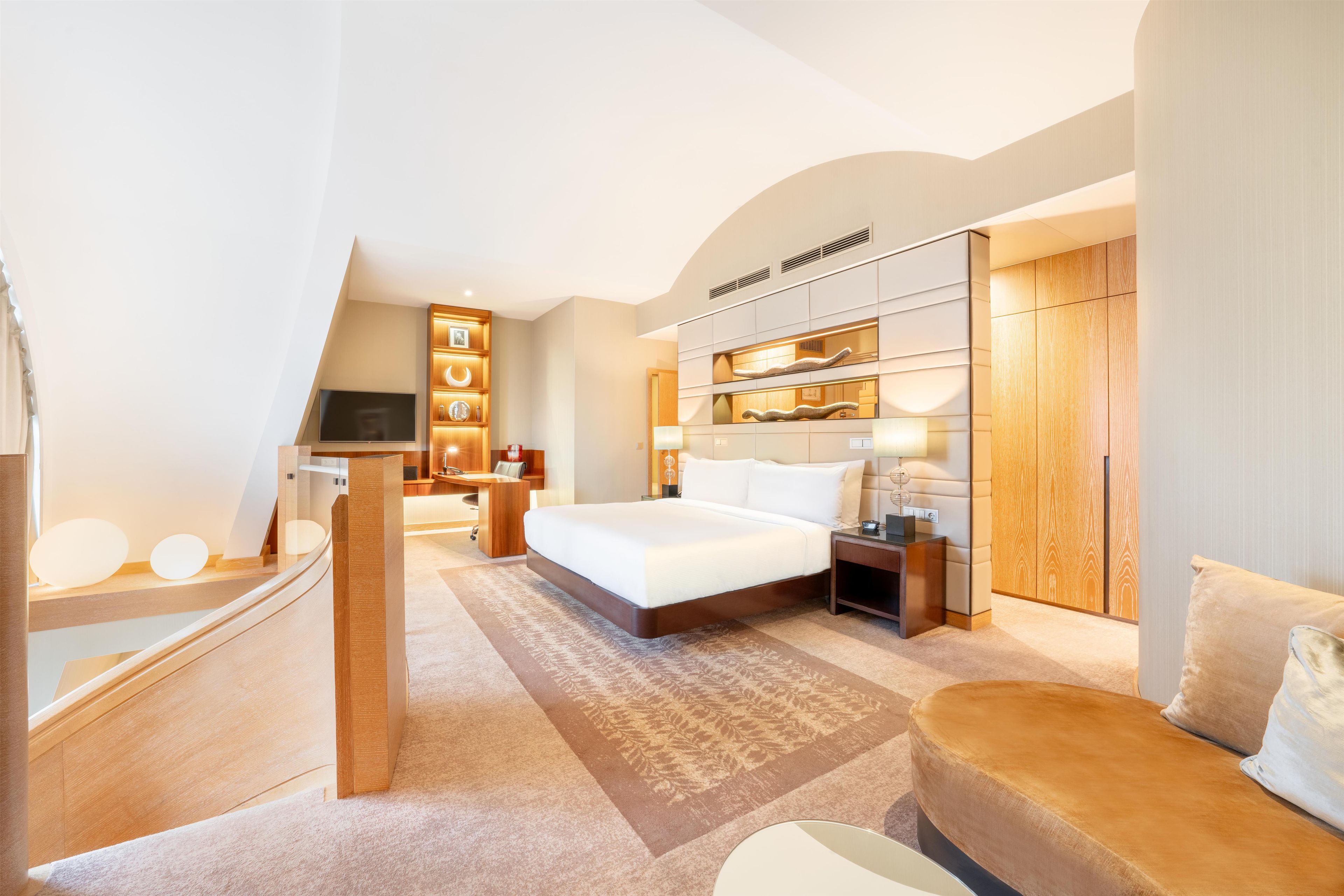 A modern hotel room with a large bed, a desk, a wardrobe, and a TV.