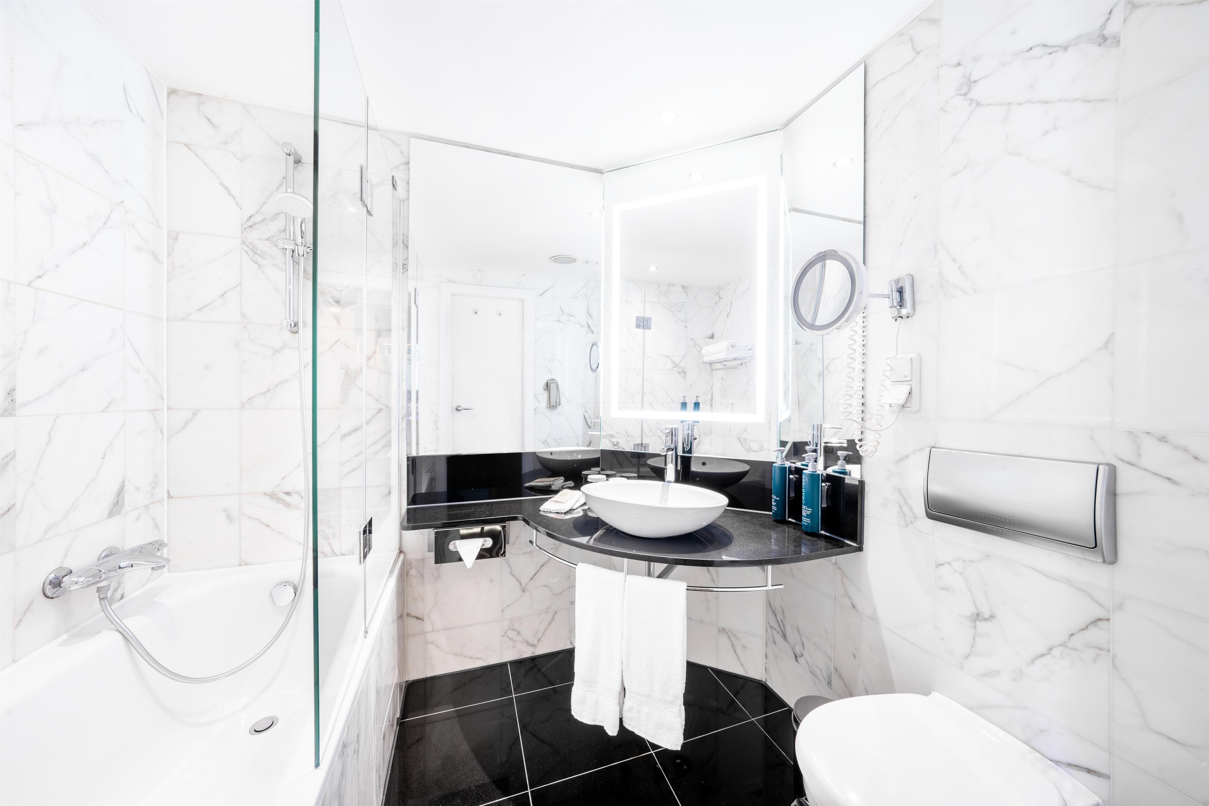 A modern bathroom with a glass-enclosed shower, a black and white marble sink, and a toilet.