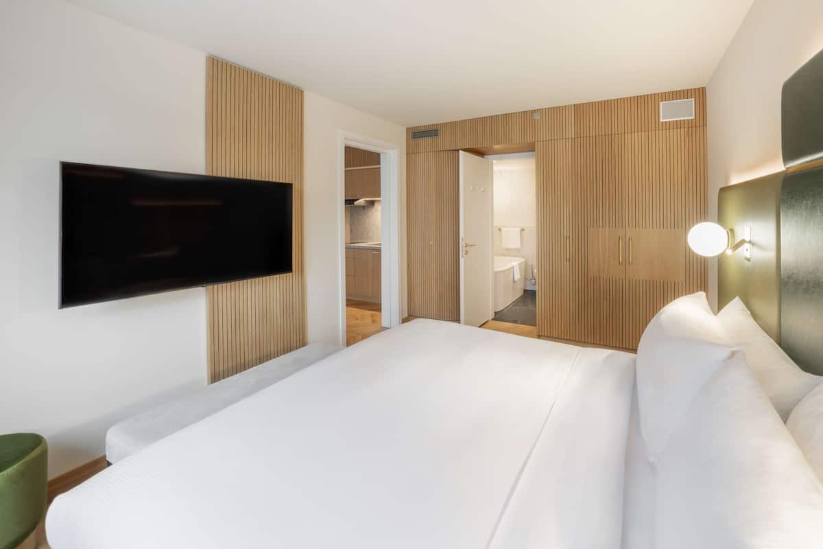 A modern hotel room with a large bed, a flat-screen TV mounted on the wall, and a walk-in closet with sliding doors.