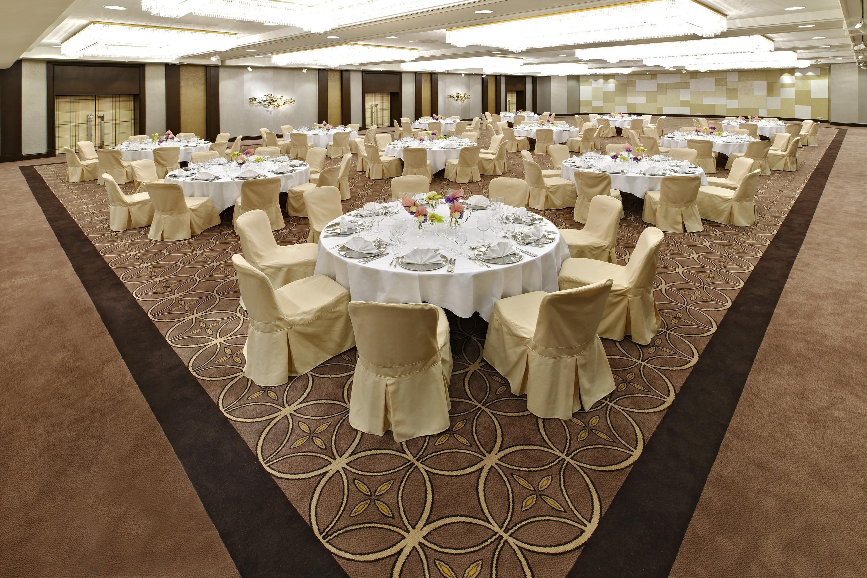Un salón de banquetes con mesas redondas dispuestas para comer, rodeado de sillas con fundas blancas.