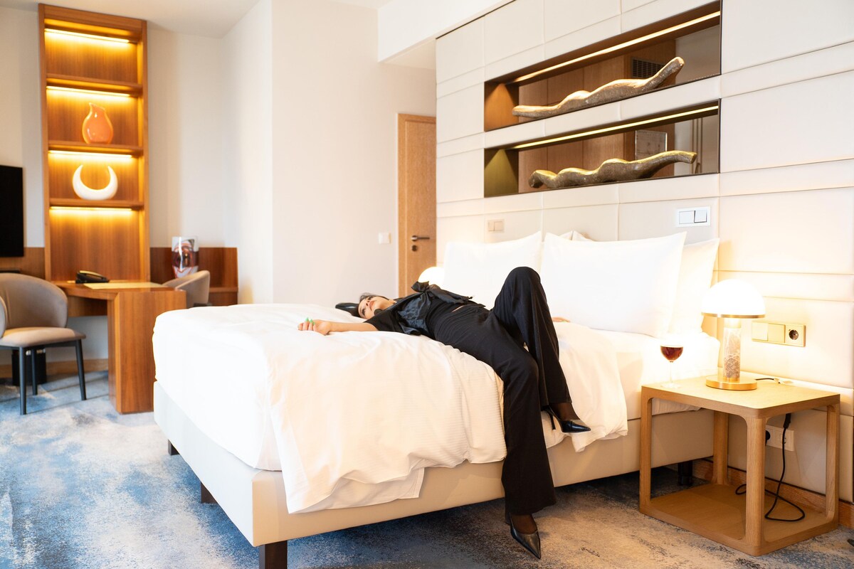 Una camera d'albergo con un letto, un comodino, una lampada e una scrivania con una sedia.