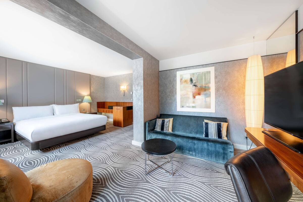 A modern hotel room with a large bed, a sofa, a TV, and a desk.