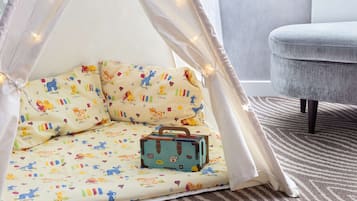Ein gemütliches Zimmer mit einem Bett mit farbigem Tierprint, einem kleinen blauen Koffer und einem grau gepolsterten Sessel.