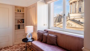 A room with a window overlooking a historic building, a cushioned bench, and built-in shelving.