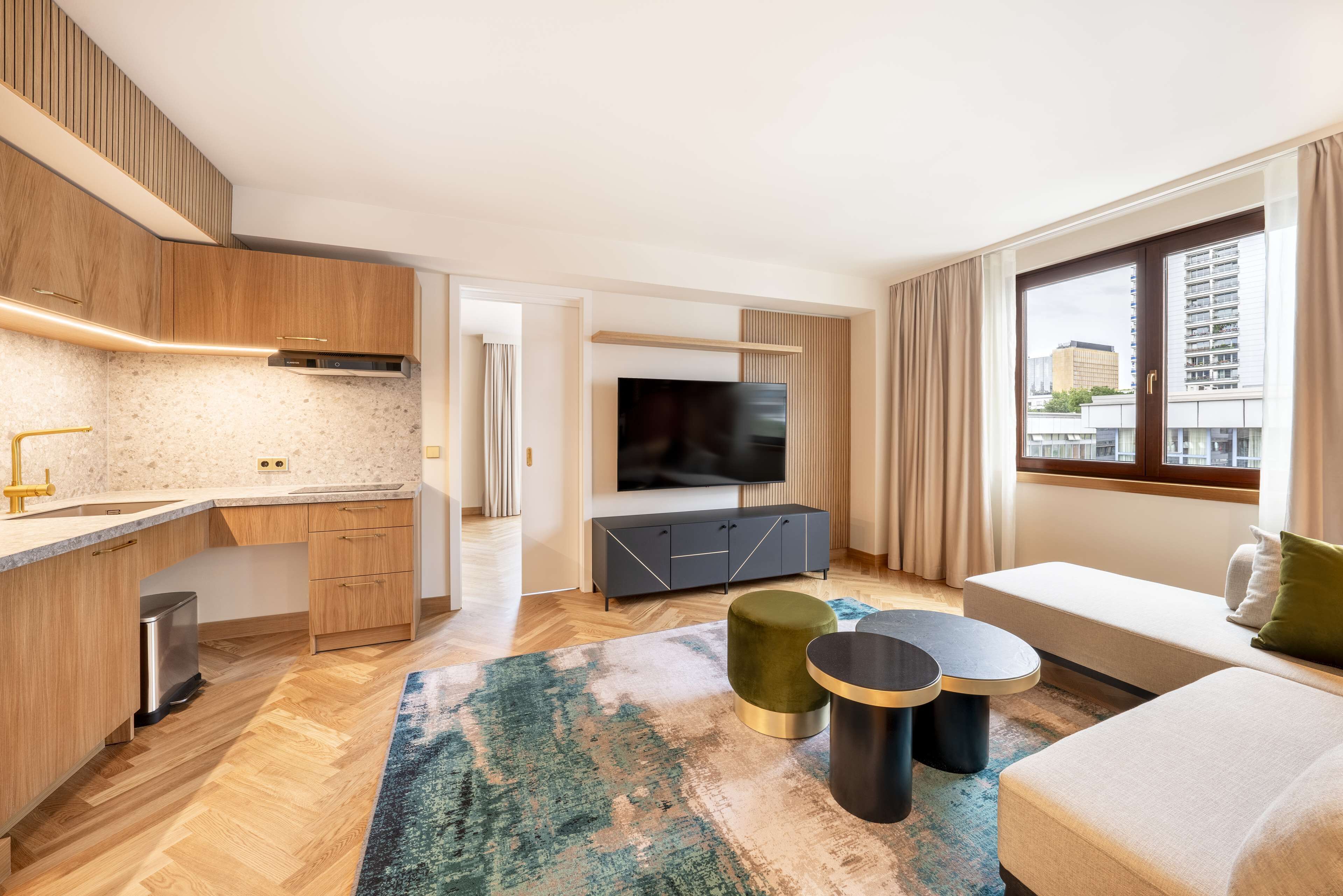 Een moderne woonkamer met een bank, een televisie en een keukenhoek met houten kasten en een aanrecht.