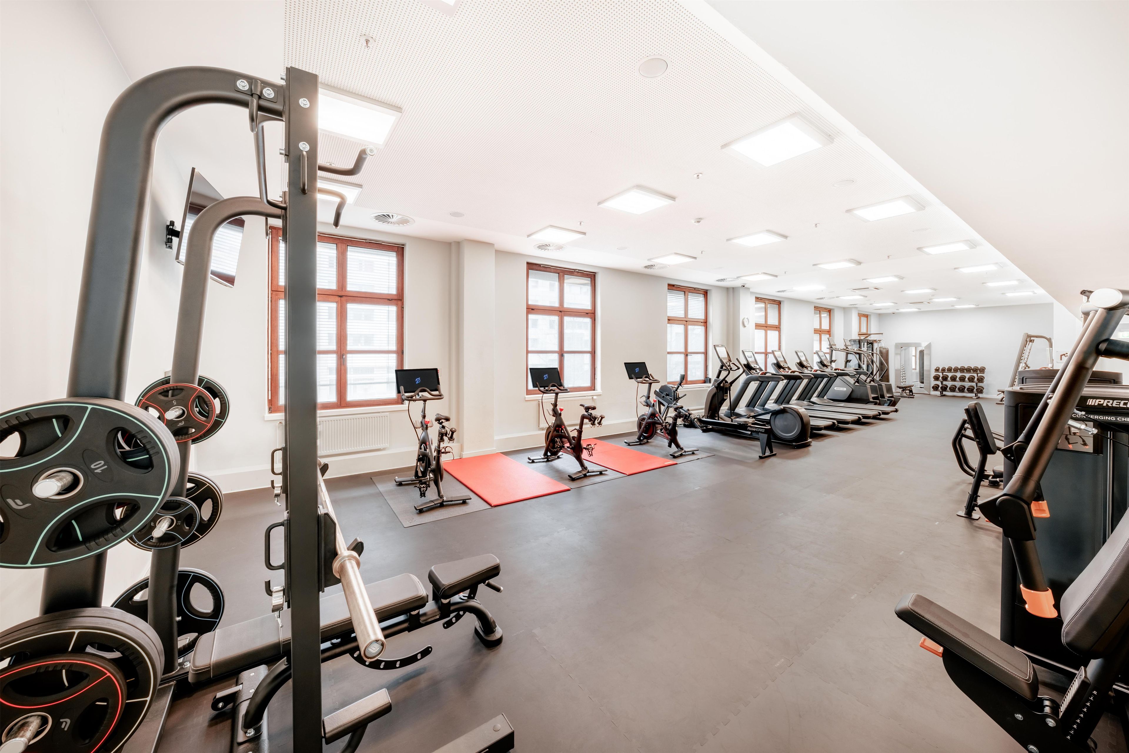 A gym with various exercise equipment, large windows, and a high ceiling.