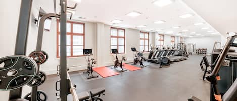 A gym with various exercise equipment, large windows, and a high ceiling.