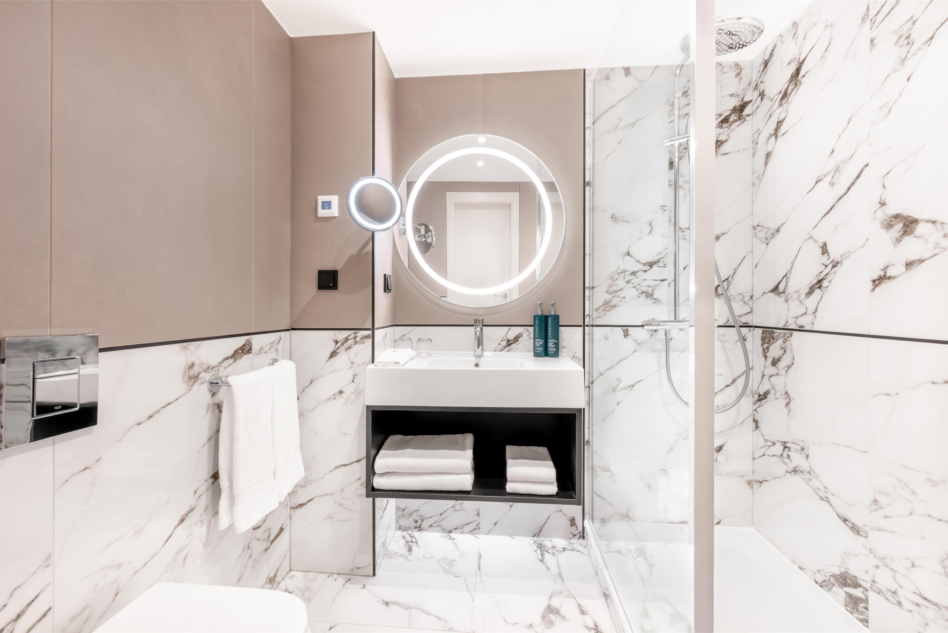 A modern bathroom with a marble vanity, a built-in sink, a mirror with a light, and a shower area.