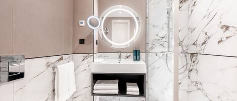 A modern bathroom with a marble vanity, a built-in sink, a mirror with a light, and a shower area.