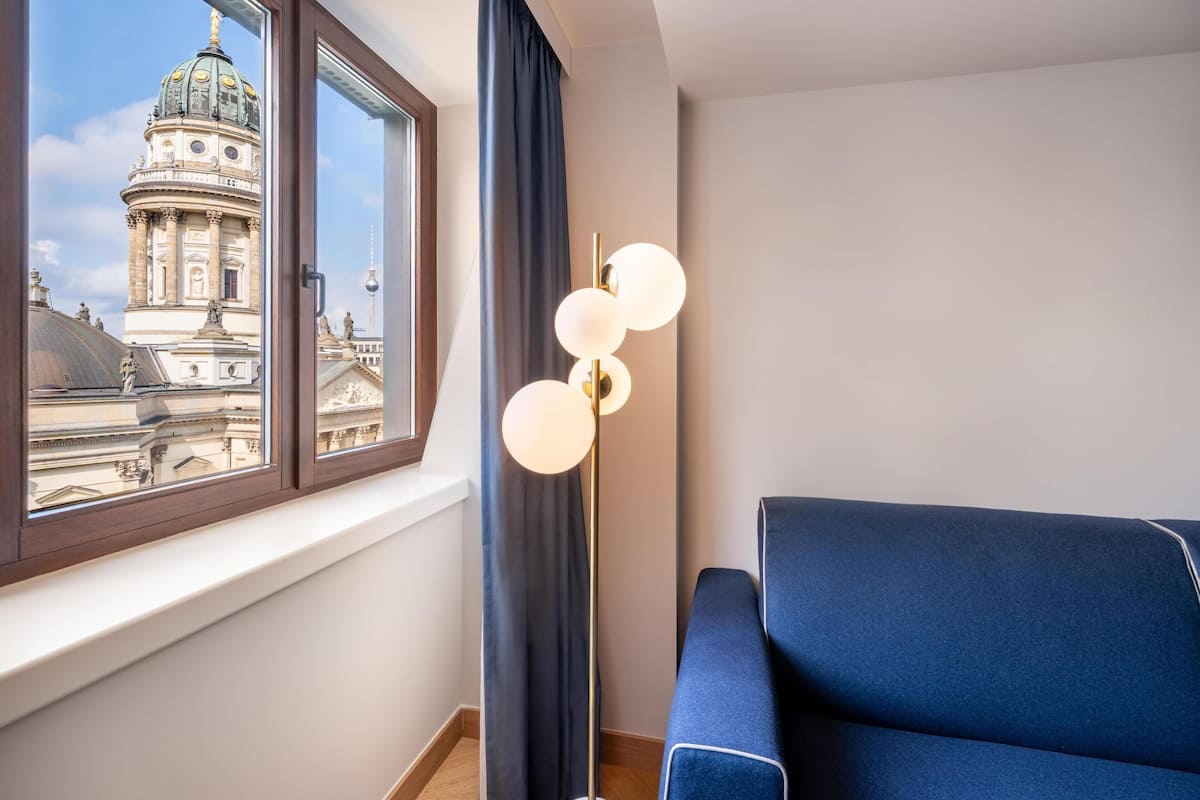 A room with a view of a historic building through a window, a blue sofa, and a modern floor lamp.