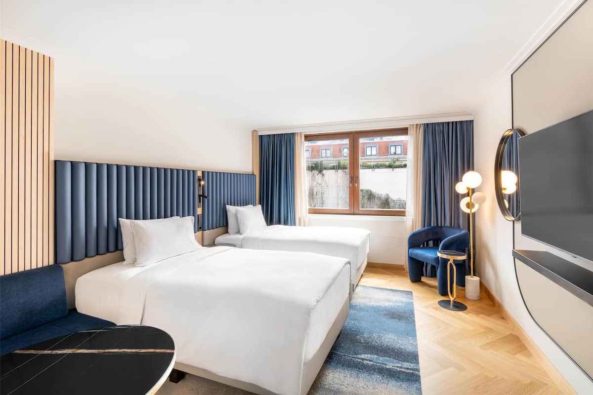 A hotel room with two beds, a sofa, a TV, and a window with curtains.