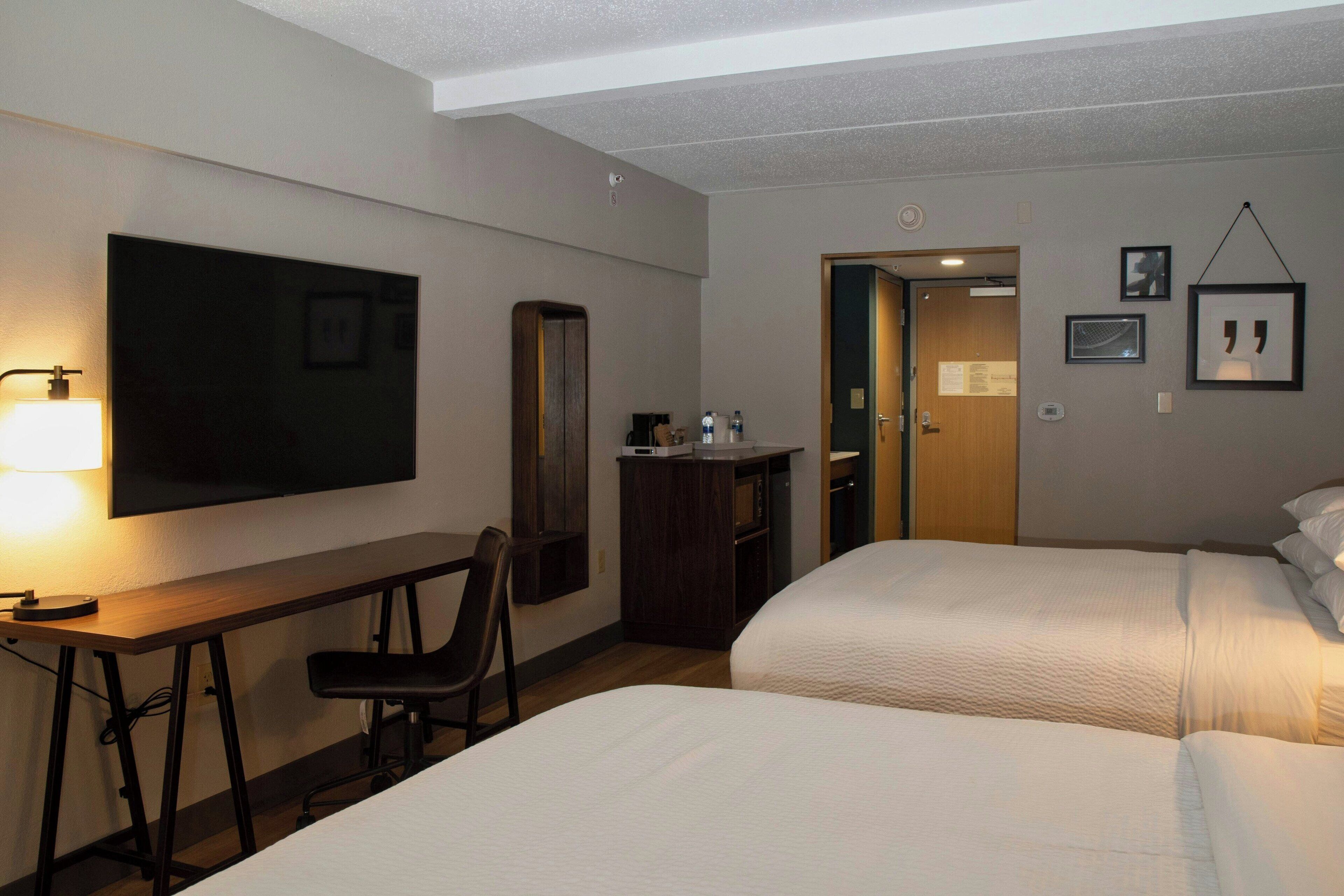 A hotel room with a desk, two beds, a TV, and a door leading to a bathroom.