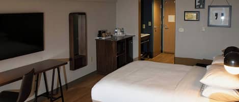 Habitación de hotel con dos camas, un escritorio, una silla, un televisor, un espejo y una puerta que da al baño.