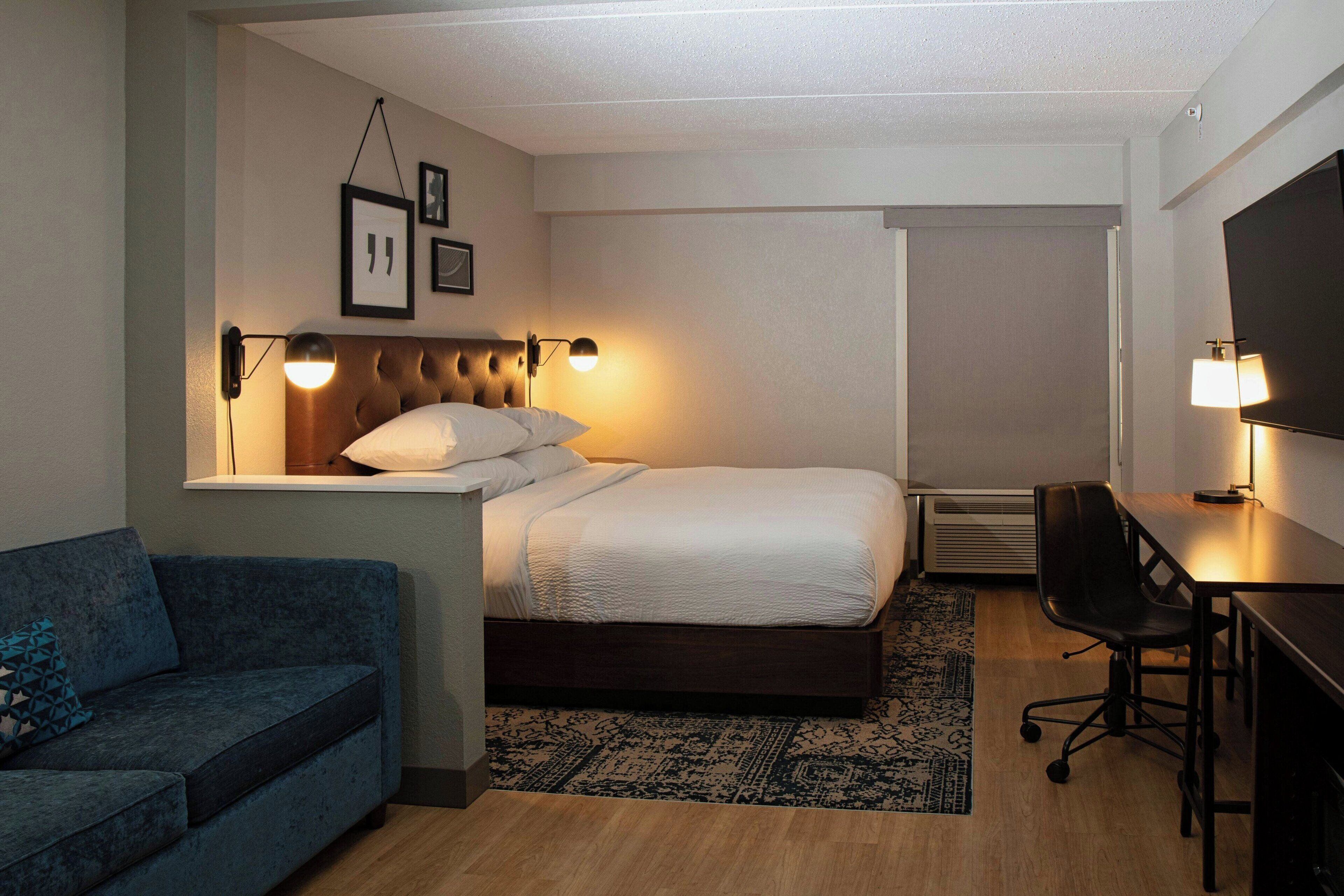 Una habitación de hotel con cama, escritorio, silla, sofá y televisor.