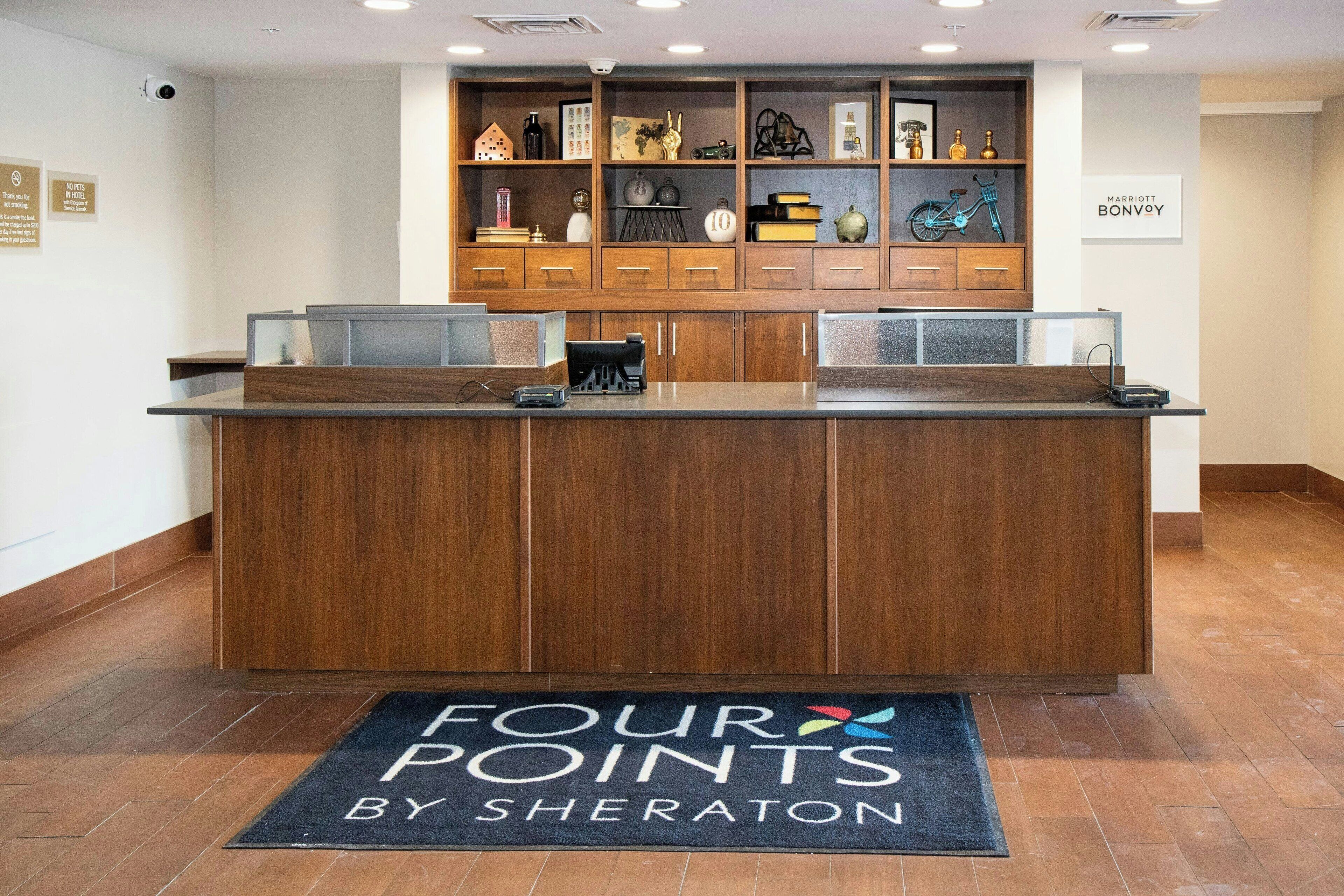 En receptionsdisk med træfinish, en sort måtte med teksten "FOUR POINTS BY SHERATON", og et "MARRIOTT BONVOY" skilt på væggen.