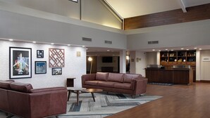 Un hall d’entrée spacieux, avec un canapé en cuir marron, une table basse et un coin bar doté de meubles en bois.