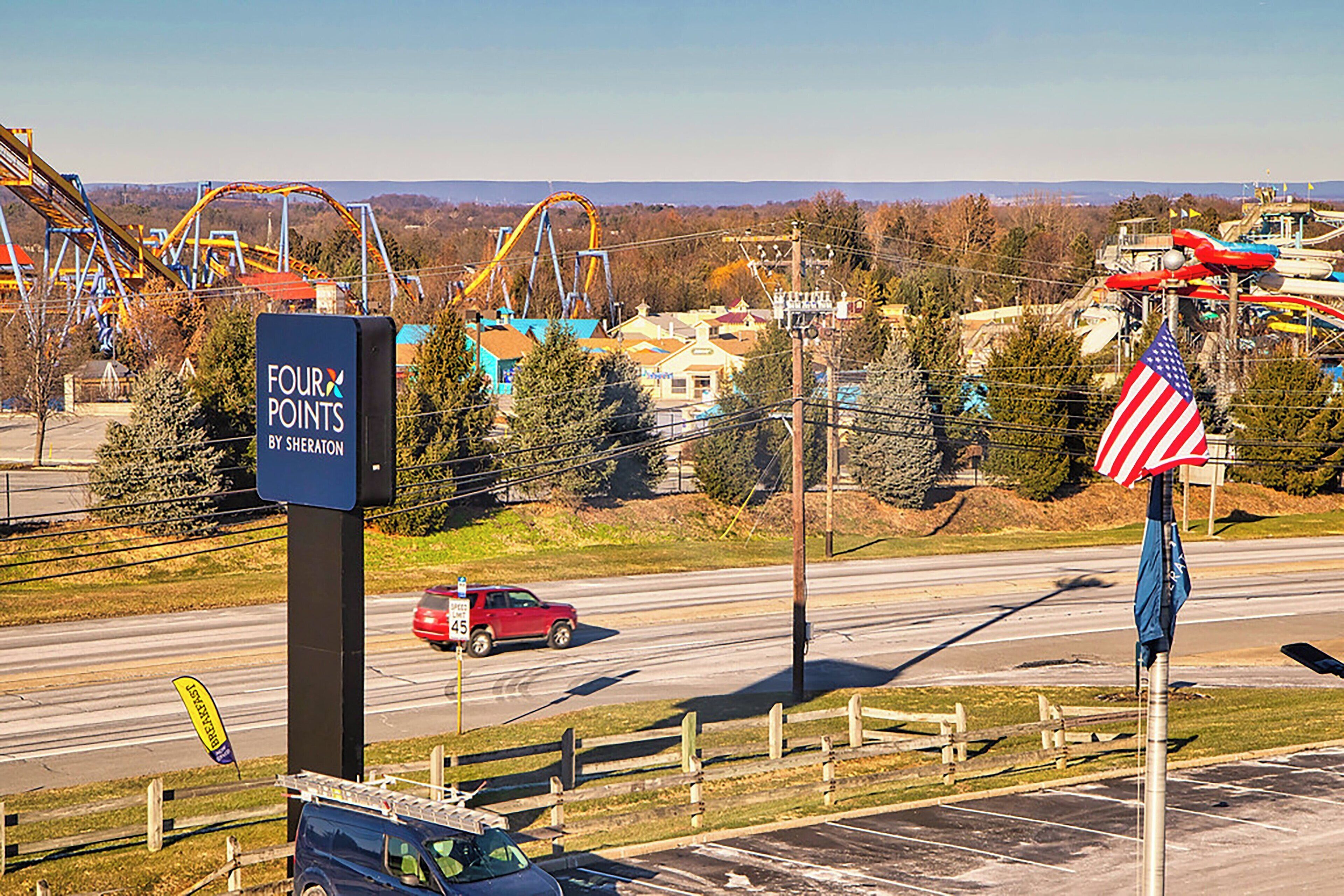 A sign for 'Four Points by Sheraton' with a view of amusement park rides and a road with a red car.