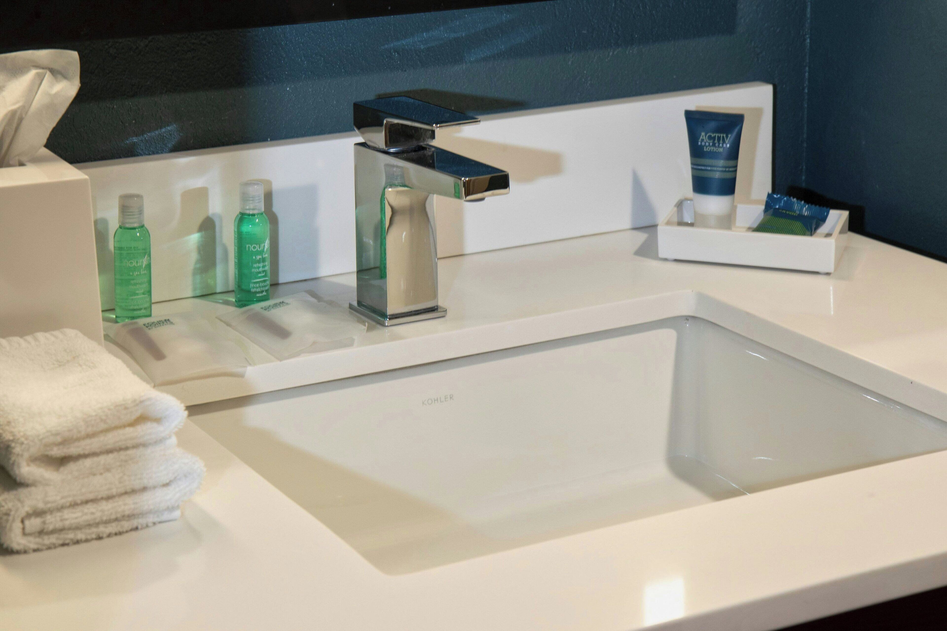 Un baño de hotel con un lavamanos moderno, artículos de tocador y toallas.