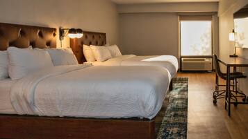 A hotel room with two beds, a desk, and a window with a view of trees.