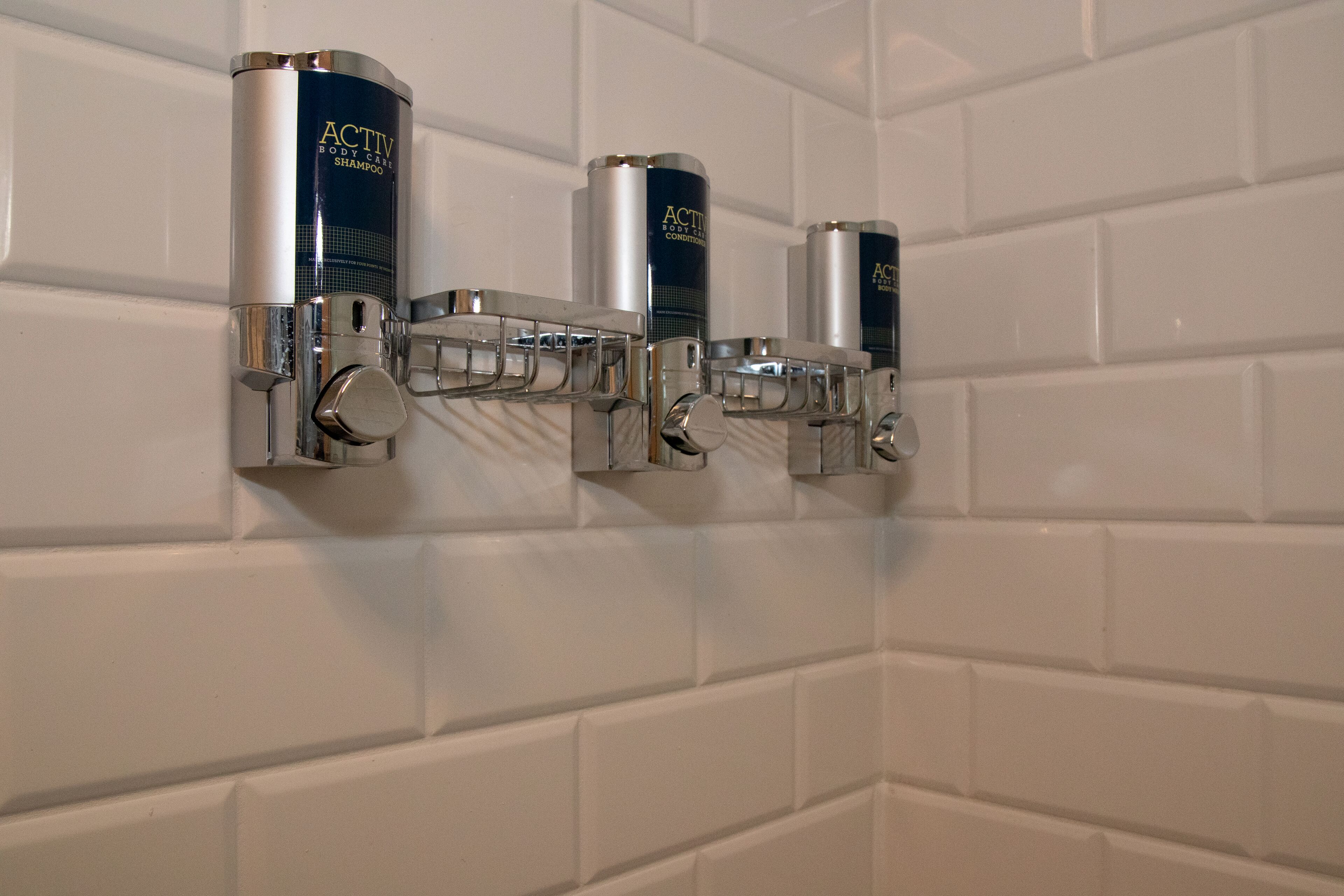 Un distributeur mural contenant trois flacons de shampoing pour le corps de la gamme ACTIV.