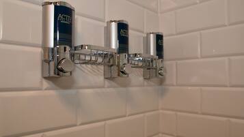 A wall-mounted dispenser with three bottles of ACTIV body care shampoo.
