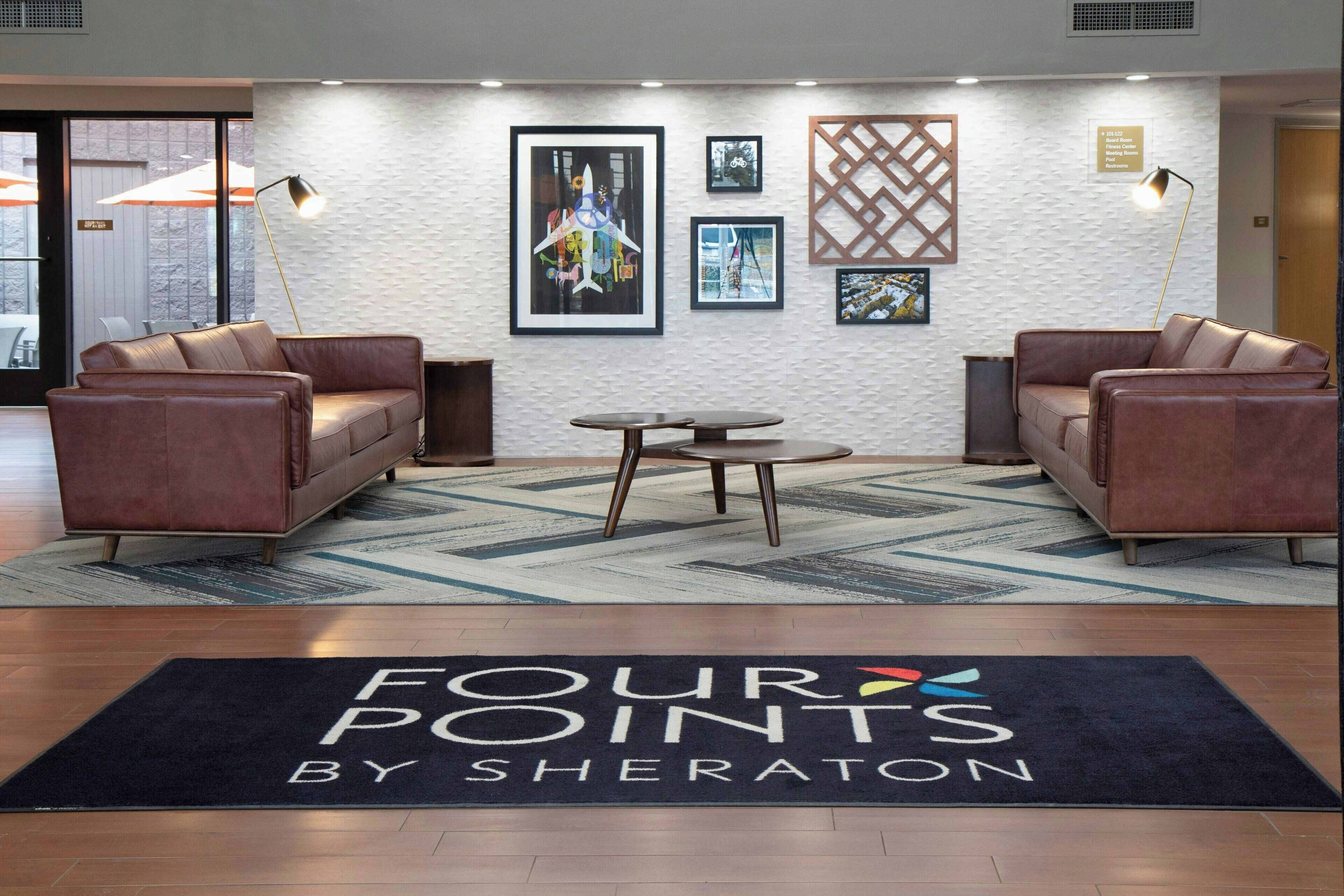 A lobby with two leather sofas, a small round table, and a black rug with "FOUR POINTS BY SHERATON" text.