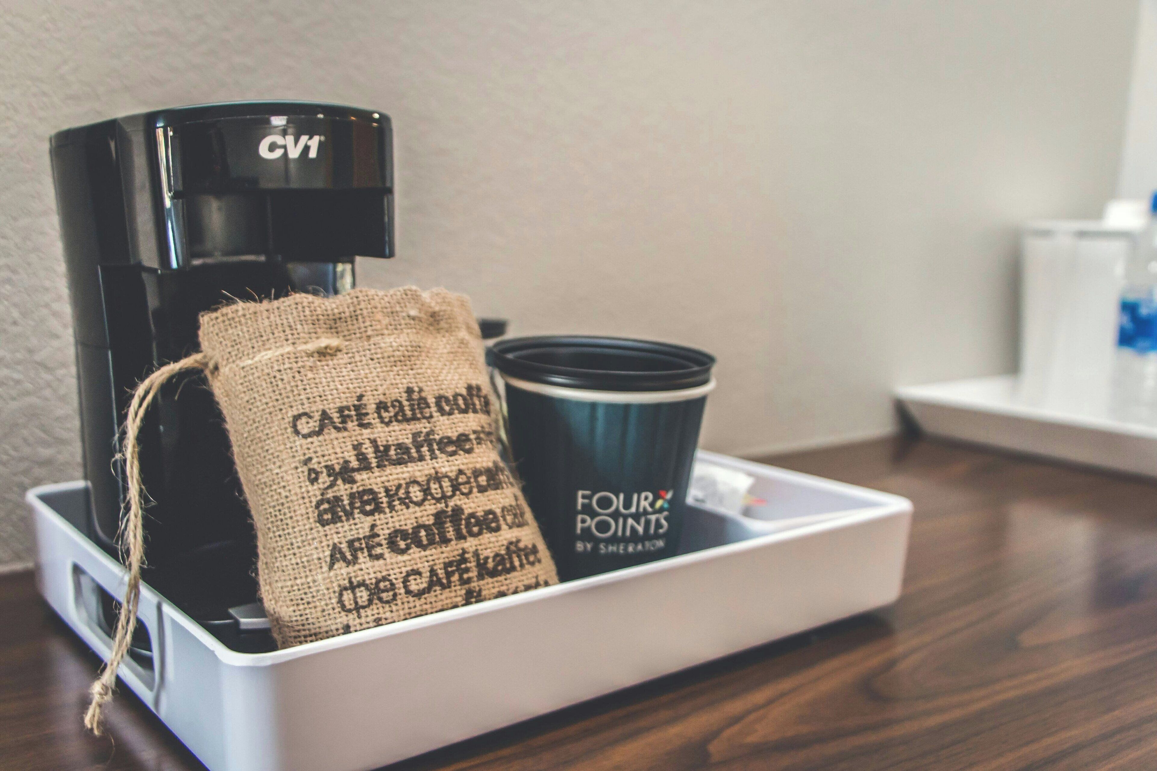 A coffee maker, a burlap sack, and a cup on a tray.