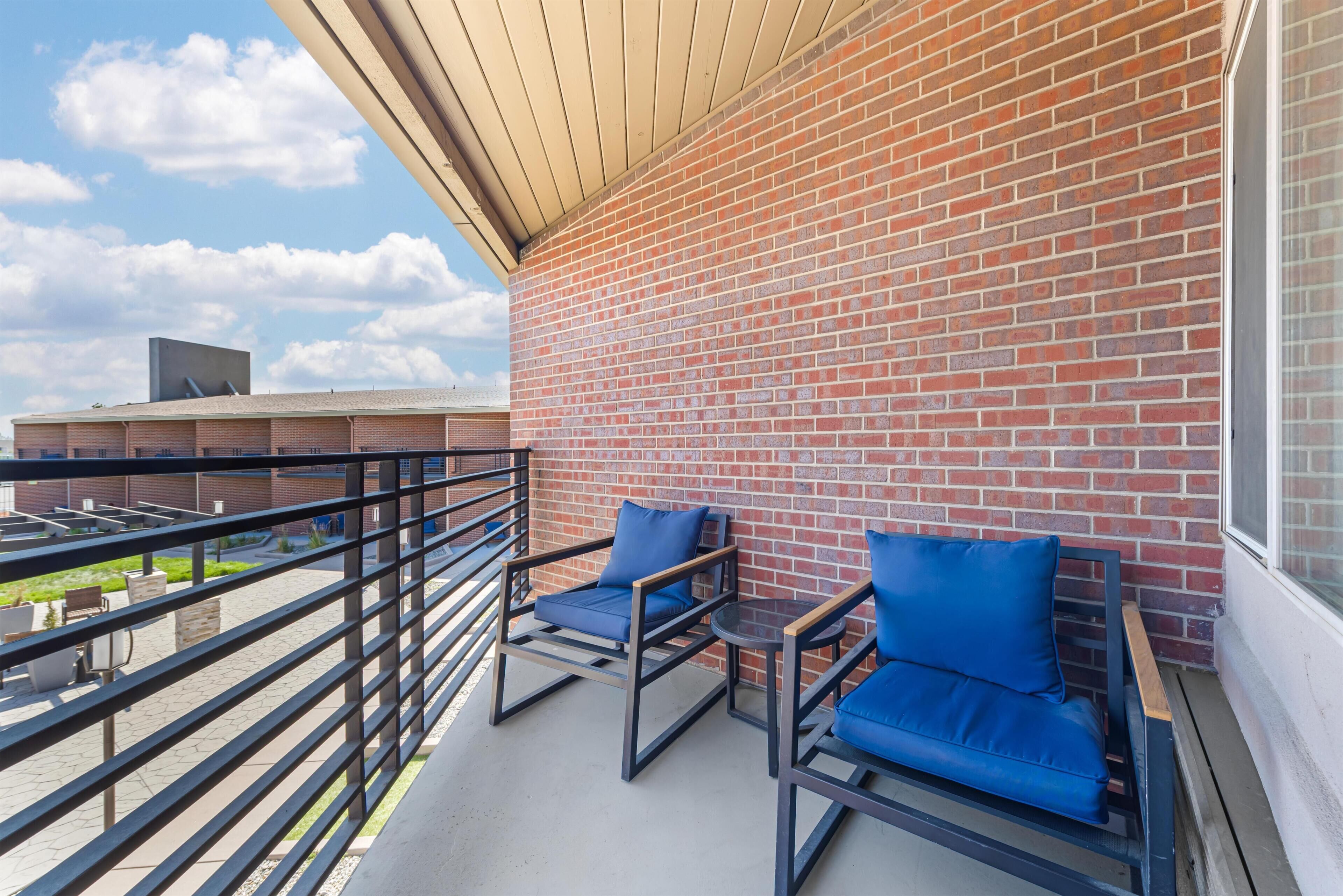 A balcony with two blue cushioned chairs, a small round table, and a brick wall.