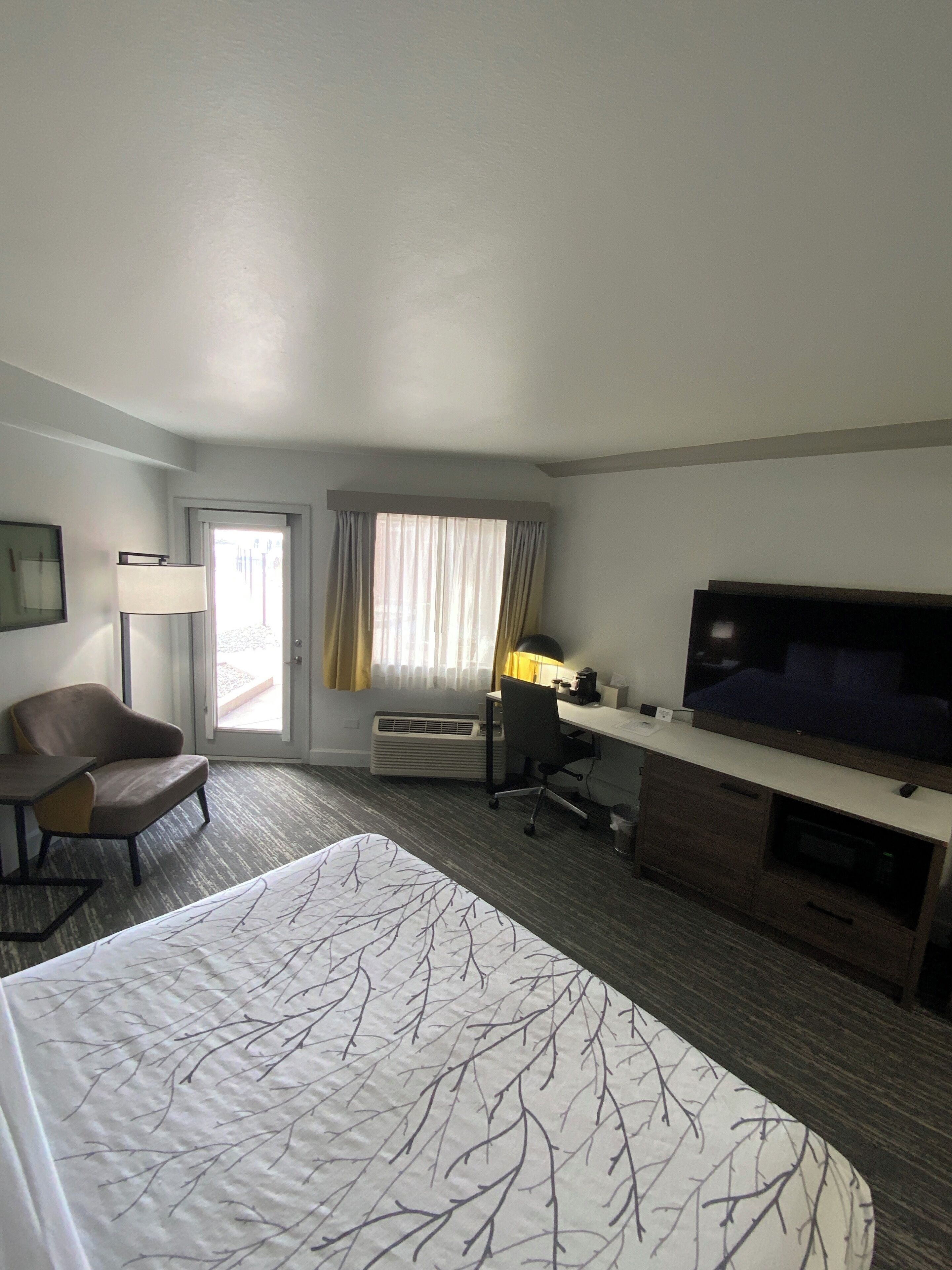 A hotel room with a bed, a desk, a chair, a television, and a window with curtains.