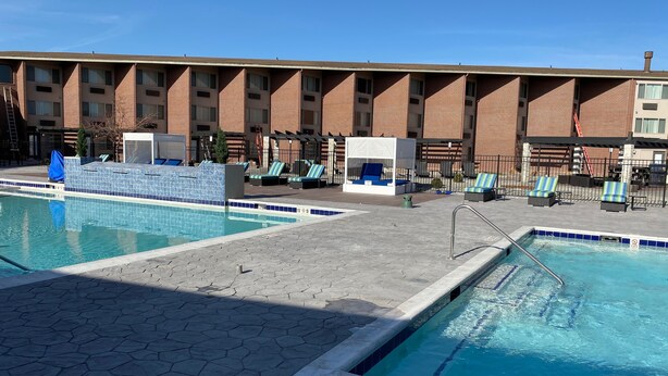 A swimming pool with lounge chairs and a covered seating area, surrounded by a brick building with multiple windows.