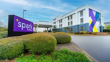 Un hotel moderno con un cartel que dice 'spark by Hilton', rodeado de setos cuidados y un cielo despejado.