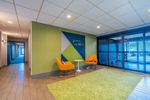 A modern lobby with a green wall, two orange chairs, a small white table, and a large window. - Spark by Hilton Atlanta Kennesaw Town Center (Kennesaw)