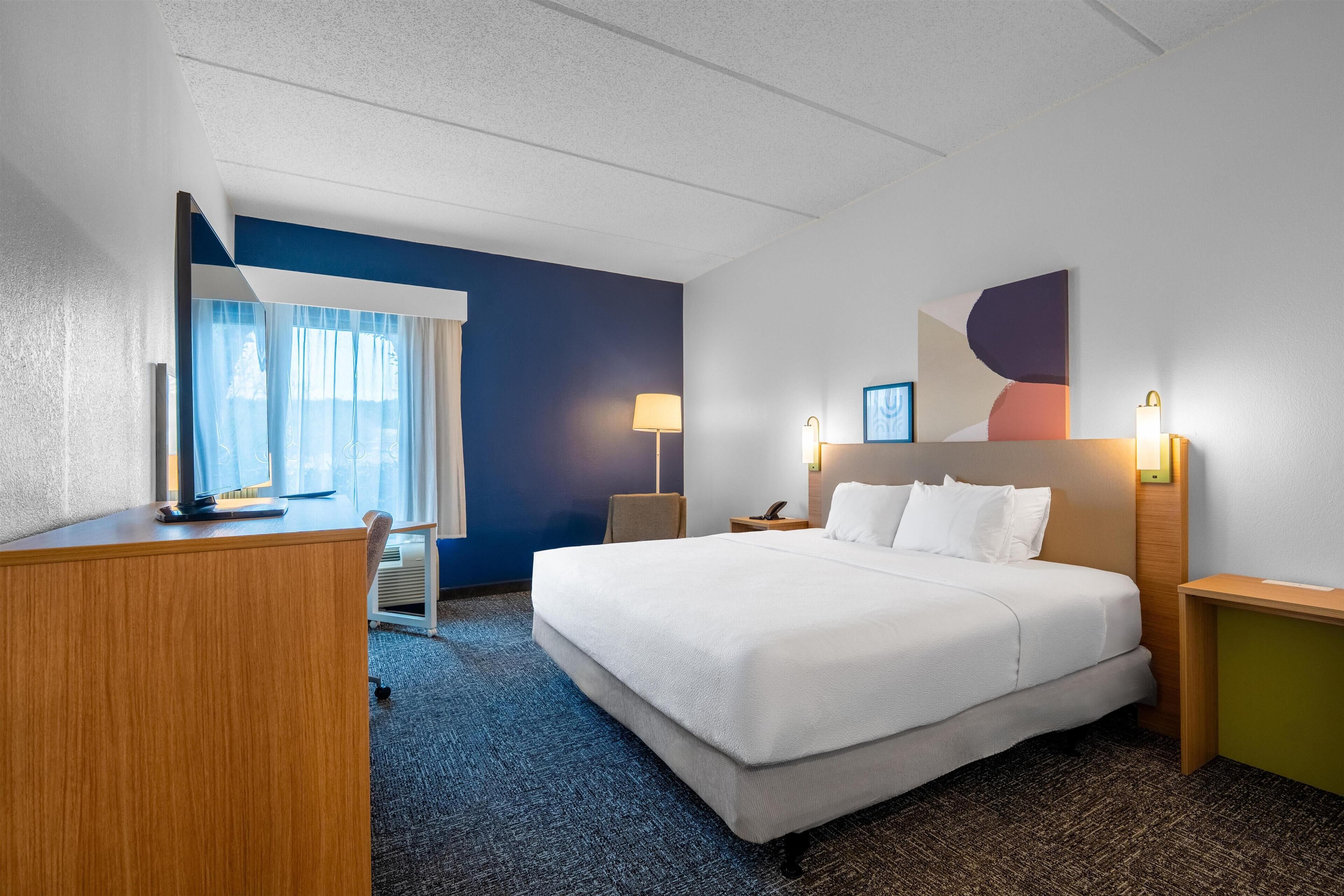 Een hotelkamer met een bed, bureau, stoel en een raam met gordijnen.